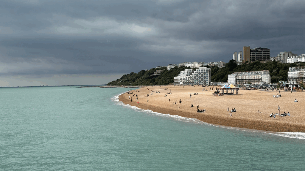 Gloomy skies on the horizon while people are enjoying the sandy beach and blue sea in the UK. Dealing with uncertainty on the beach or in business,