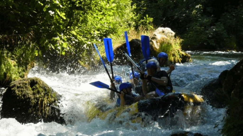 Whitewater rafting, 7 people on a yellow raft with their paddles in the air as they negotiate river rapids 